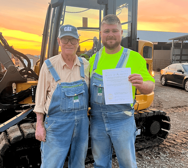 Jesse Wilkins and his Paw Paw Douglas Wilkins in front of a CAT excavator at sunset