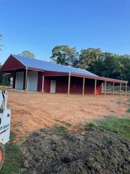 Red metal pole barn on a completed dirt pad under blue sky