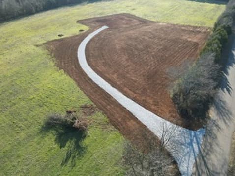 Aerial view of a sweeping gravel driveway through a red clay field
