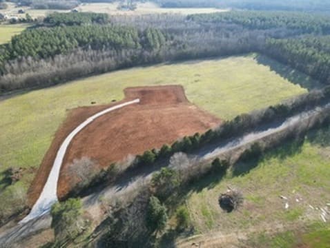 Aerial view of a completed house pad and gravel driveway through a green field