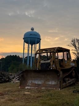Old bulldozer at sunset with Moulton water tower and dramatic orange sky behind