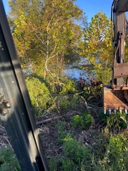Land clearing along a waterway using an excavator in autumn foliage