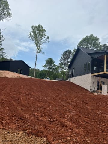 Red graded mound beside a home under construction surrounded by tall pines