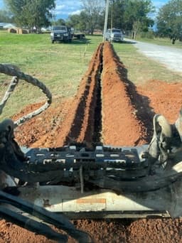 Freshly cut red clay trench running straight down a job site