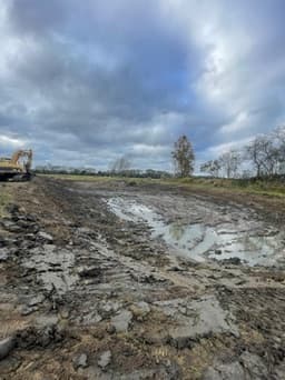 Wide muddy excavation work in progress with standing water and an excavator in the distance
