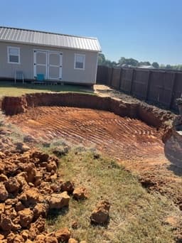 Freshly dug rectangular backyard pond excavation with ribbed red clay walls