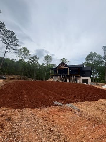 Graded red clay house pad with a craftsman home under construction in the background