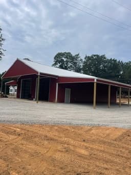 Completed red metal pole barn on a finished dirt and gravel pad