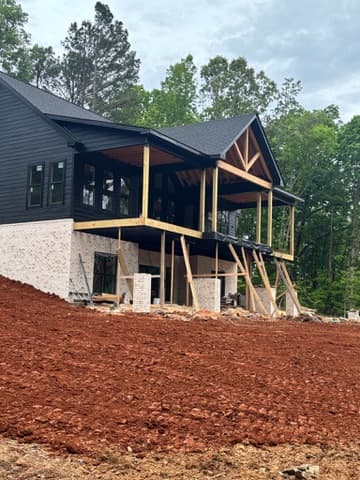 House under construction with graded red clay pad and tall pines behind