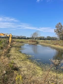 Excavator digging a pond channel through an open field
